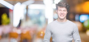 Arka plan eller üzerinde kış kazak giyen genç yakışıklı adam birlikte izole ve rahat ve neşeli gülümseyen parmak çarpı işareti. Başarı ve iyimser