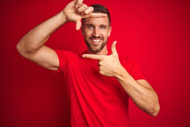 Genç yakışıklı adam kırmızı izole arka plan üzerinde rahat t-shirt giyen mutlu yüzü ile elleri ve parmakları ile çerçeve yapma gülümseyerek. Yaratıcılık ve fotoğrafçılık konsepti.