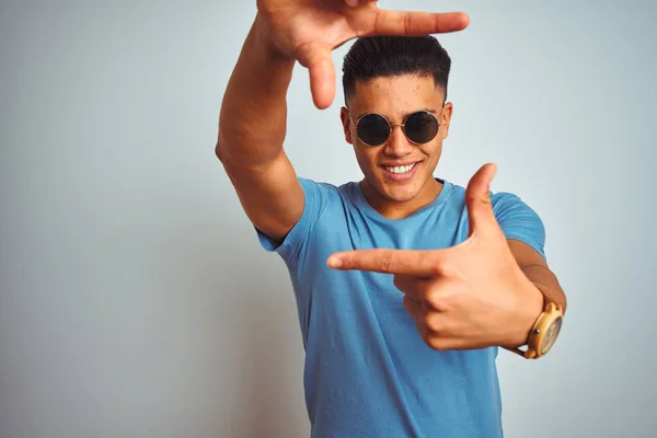 年轻的巴西男子穿着蓝色T恤和太阳镜在孤立的白色背景微笑 用手和手指与快乐的脸框 创意与摄影理念 — 图库照片