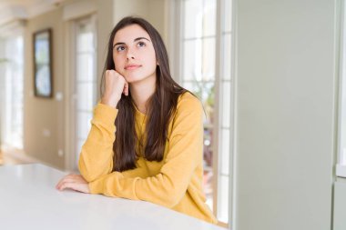 Çene düşünme hakkında soru, dalgın ifade üzerine el ile sarı kazak giyen güzel genç kadın. Düşünceli yüzüyle gülümsüyor. Şüphe kavramı.