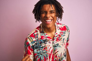 Tatilde dreadlocks ile Afro adam izole pembe arka plan üzerinde çiçek gömlek giyen çok mutlu ve heyecanlı kolları kaldırdı ile kazanan jest yapıyor, gülümseyen ve başarı için çığlık. Kutlama konsepti.