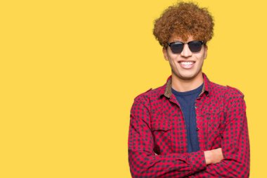 Kameraya bakarak çapraz silah ile gülümseyen güneş gözlüğü mutlu yüz giyen afro saçlı Genç yakışıklı adam. Olumlu bir kişi.