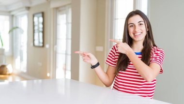 Rahat çizgili t-shirt giyen güzel genç kadın gülümseyerek ve yan iki el ve parmakları ile işaret kamera bakıyor.