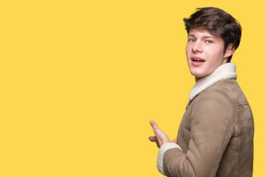 Açık el ile doğal gülümseyen girmek için izole arka plan davet üzerine kış ceket giyen genç yakışıklı adam