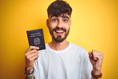 Izole sarı arka plan üzerinde İtalya İtalyan pasaportu giyen dövme ile genç adam gurur çığlık ve zafer ve başarı kutluyor çok heyecanlı, duygu tezahürat