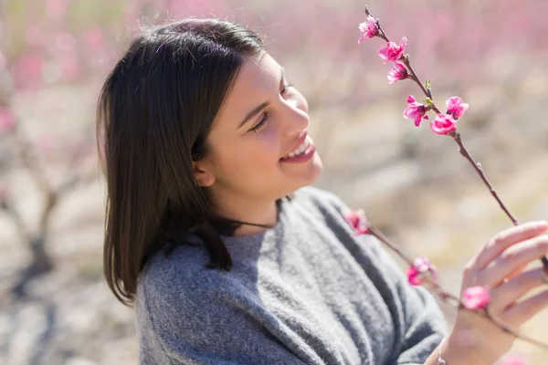 Hermosa joven sonriendo alegre en un jardín de melocotón con pi —  Fotos de Stock