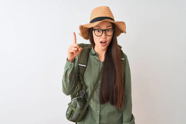 Chinese hiker woman wearing canteen hat glasses backpack over isolated white background pointing finger up with successful idea. Exited and happy. Number one.