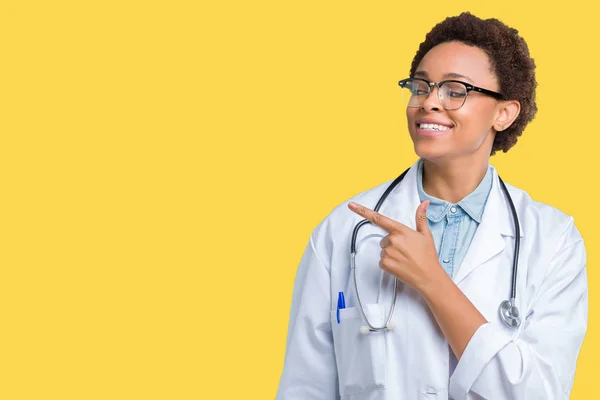 手と顔に幸せで自然な表現のある側までの指で指している顔の笑顔で陽気な孤立した背景に医療のコートを着ている若いアフリカ系アメリカ人医師女性 — ストック写真