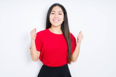 İzole arka plan üzerinde kırmızı t-shirt giyen güzel esmer kadın şaşırmış ve kollarını kaldırdı ve açık gözleri ile başarı için şaşırttı. Kazanan kavramı.