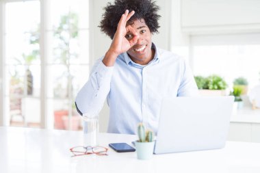 Afrika kökenli Amerikalı iş adamı mutlu yüz el parmaklarının arasından seyir göz üzerinde ok işaretiyle yapıyor gülümseyen ile dizüstü bilgisayar kullanarak çalışma