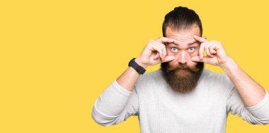 Rahat kazak giyen genç sarışın adam parmaklarıyla gözleri açmaya çalışıyor, uykulu ve yorgun sabah yorgunluğu için