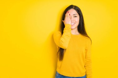 Yüzünde kendine güvenen bir gülümseme ve sürpriz duygu ile el ile bir göz kapsayan sarı izole arka plan üzerinde güzel esmer kadın.