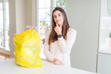 Çöp konteynerinden çöpü çıkararak çenesini eliyle sorguladığını düşünen genç kadın, dalgın ifadesini kullandı. Düşünceli bir yüzle gülümsüyor. Şüphe kavramı.