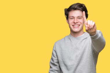 Ve kendinden emin ve mutlu gülümseyerek süre parmak numaralı yukarıyı gösteren izole arka plan üzerinde sweatshirt giyen genç yakışıklı sportif adam.