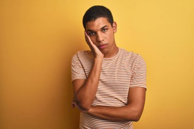 Genç yakışıklı arap adam çizgili t-shirt izole sarı arka plan üzerinde duran giyen yorgun görünümlü ve çapraz kolları ile depresyon sorunları ile sıkılmış düşünme.