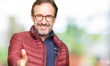 Orta yaş yakışıklı adam gözlük ve kış ceket tebrik ve davet edici olarak gülümseyen dostu sunan el sıkışma. Başarılı iş.