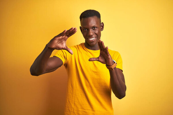 Young african american man wearing casual t-shirt standing over isolated yellow background doing frame using hands palms and fingers, camera perspective