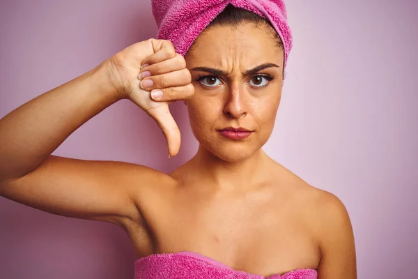 Young beautiful woman wearing towel after shower over isolated pink background with angry face, negative sign showing dislike with thumbs down, rejection concept