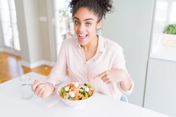 Young african american woman eating healthy pasta salad very happy pointing with hand and finger