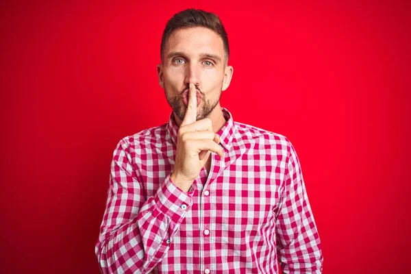 Kırmızı izole arka plan üzerinde genç yakışıklı adam dudaklarında parmak ile sessiz olmak isteyen. Sessizlik ve gizli kavram.