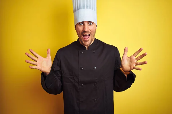 年轻的厨师男子穿着制服和帽子站在孤立的黄色背景庆祝疯狂和惊讶的成功与手臂抬起和睁开眼睛尖叫兴奋 优胜者概念 — 图库照片