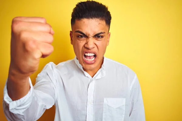 Young brazilian businessman wearing elegant shirt standing over isolated yellow background annoyed and frustrated shouting with anger, crazy and yelling with raised hand, anger concept