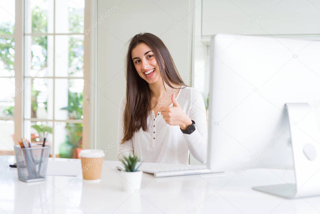 Beautiful young woman working using computer doing happy thumbs up gesture with hand. Approving expression looking at the camera with showing success.