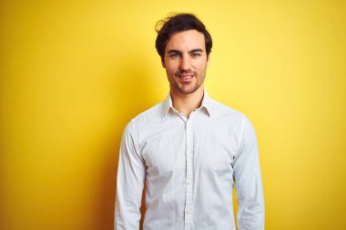 Genç yakışıklı işadamı yüzünde mutlu ve serin bir gülümseme ile izole sarı arka plan üzerinde duran zarif gömlek giyiyor. Şanslı kişi.