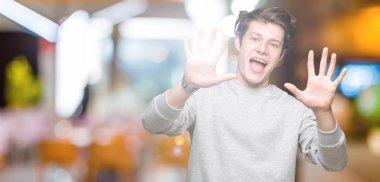 Gösterilen arka plan üzerinde sweatshirt giyen genç yakışıklı sportif adam izole ve parmakları ile işaret kendinden emin ve mutlu gülümseyerek süre on numara.