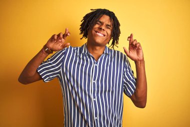 Izole sarı arka plan gesturing parmak üzerinde rahat çizgili t-shirt giyen dreadlocks ile Afro adam umut ve gözleri kapalı gülümseyerek geçti. Şans ve batıl kavram.