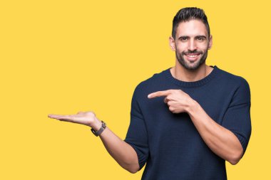 Hayret ve el ile sunulması ve parmak ile işaret ederken kameraya gülümseyen izole arka plan üzerinde kazak giyen genç yakışıklı adam.