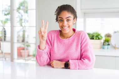 Afro saçlı güzel afro-amerikan kadın rahat pembe kazak gösteren ve parmakları ile işaret ederken emin ve mutlu gülümseyerek iki numara.