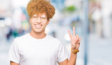 Mutlu yüz zafer işareti yaparken kameraya göz kırpıyor ile gülümseyen gözlüklü afro saçlı Genç yakışıklı adam. İki numaralı.