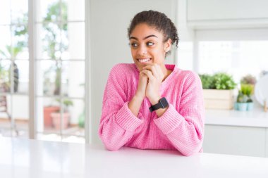 Afro saçlı güzel afro-amerikan kadın rahat pembe kazak sinirli gülüyor ve yan bakan çene elleri ile heyecanlı