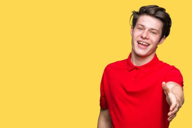 Tebrik ve konuksever dost sunan karşılıklı gülümseyen izole arka plan üzerinde kırmızı t-shirt giyen genç yakışıklı adam. Başarılı iş.