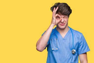 Genç doktor gülümseyen, parmakları ile mutlu yüz üzerinden seyir göz el ile ok jest yapıyor izole arka plan üzerinde tıbbi üniforma.