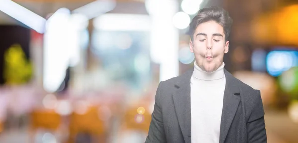 stock image Young elegant man wearing winter coat over isolated background making fish face with lips, crazy and comical gesture. Funny expression.