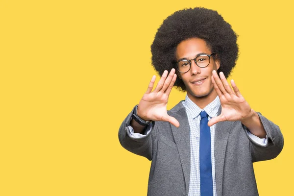 Young african american business man with afro hair wearing glasses Smiling doing frame using hands palms and fingers, camera perspective