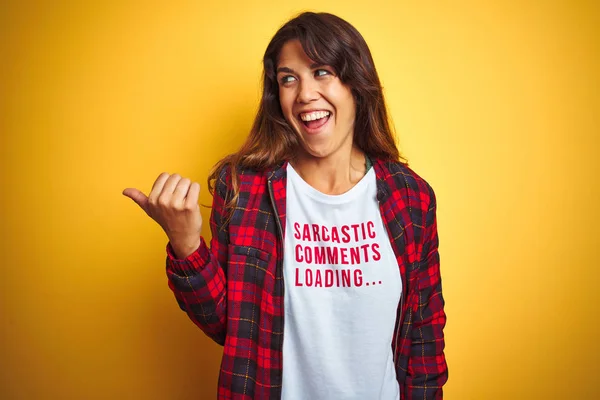 Beautiful woman wearing funny t-shirt with irony comments over isolated yellow background pointing and showing with thumb up to the side with happy face smiling