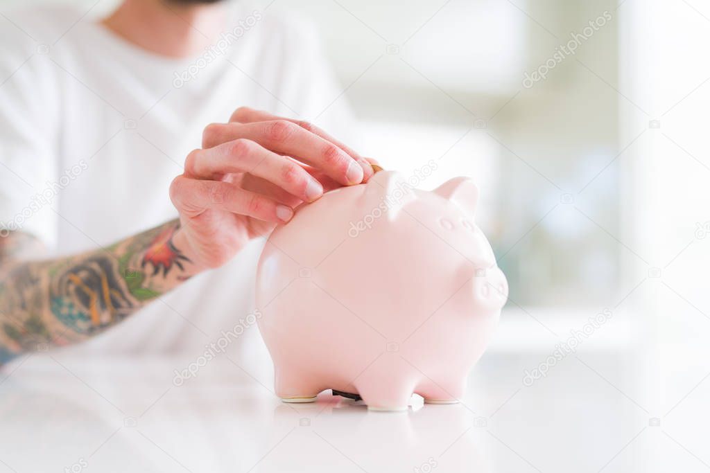 Close up of man putting a coin inside piggy bank as savings