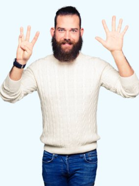 Kış kazak gösterme ve parmakları ile işaret giyen genç hipster adam numara 9 kendinden emin ve mutlu gülümseyerek süre.