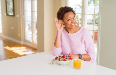 Genç afro-amerikan kadın evde sabah sağlıklı kahvaltı yapıyor el ile kulak üzerinden bir söylenti ya da dedikodu bir işitme dinleyerek gülümseyerek. Sağırlık kavramı.