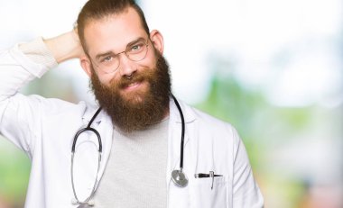 Sakal giyen tıbbi ceket ile genç sarışın doktor adam el kadar jest, çekici poz ile emin dokunmadan saç gülümsüyor