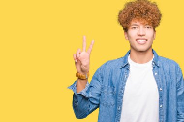 Afro saçlı genç yakışıklı adam denim ceket gösteren giyen ve emin ve mutlu gülümserken parmaksayısı iki ile işaret.