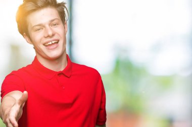 Tebrik ve konuksever dost sunan karşılıklı gülümseyen izole arka plan üzerinde kırmızı t-shirt giyen genç yakışıklı adam. Başarılı iş.