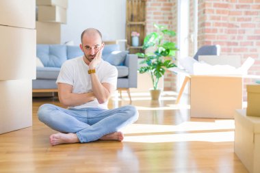 Genç kel adam karton kutular etrafında yerde oturan yeni bir eve hareketli yorgun görünümlü ve çapraz kolları ile depresyon sorunları ile sıkılmış düşünme.