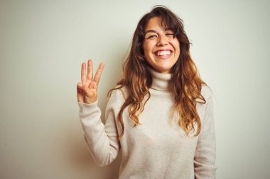 Genç güzel kadın beyaz izole arka plan üzerinde duran kış kazak giyen gösteren ve emin ve mutlu gülümserken parmakları ile üç işaret.