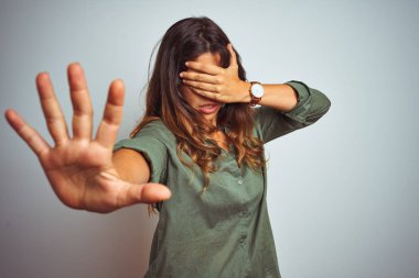 Yeşil gömlek giyen genç güzel kadın elleri ile gözleri kaplayan gri izole arka plan üzerinde duran ve üzgün ve korku ifadesi ile stop jest yapıyor. Utanmış ve olumsuz kavram.