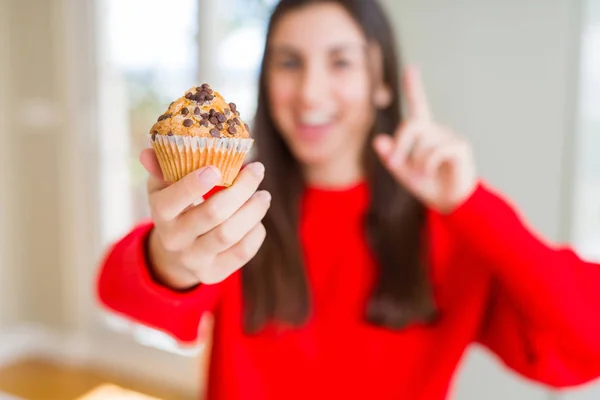 チョコレートチップマフィンを食べる美しい若い女性は 幸せな顔で指を指すアイデアや質問に驚いた ナンバーワン — ストック写真
