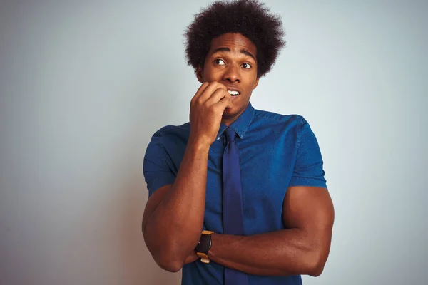 American business man with afro hair wearing blue shirt and tie over isolated white background looking stressed and nervous with hands on mouth biting nails. Anxiety problem.